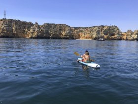 A couple enjoys paddleboarding in serene waters, surrounded by stunning coastal cliffs — a perfect day for adventure and exploration.