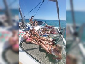 A lively group of friends enjoys sunbathing on a catamaran, sipping drinks and soaking up the sun — the perfect setting for a fun day on the water.