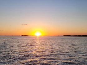 A stunning sunset over tranquil waters, creating a picturesque backdrop perfect for evening boat cruises or relaxation by the shore.