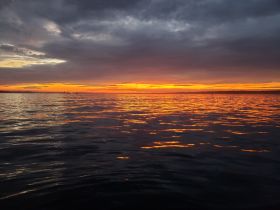 A stunning sunset casts vibrant colors over calm waters, creating a picturesque scene perfect for evening boat trips or romantic getaways.