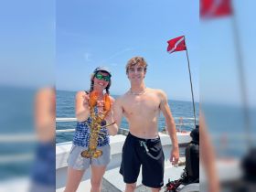 A young man and woman proudly display a freshly caught lobster while enjoying a day on the ocean — a perfect moment of celebration during their snorkeling adventure.