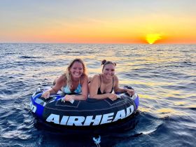 Two friends enjoy tubing in the ocean at sunset, capturing the essence of summer fun and adventure on the water.