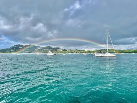 A stunning view of a sailboat under a vibrant rainbow, set against a picturesque coastline — a perfect representation of a beautiful day on the water.