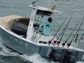 A fisherman navigates a sleek boat equipped with multiple fishing rods, showcasing an active day on the water — perfect for sport fishing enthusiasts.