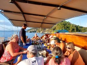 A lively group enjoys a meal on a boat, surrounded by stunning ocean views — perfect for social gatherings and dining experiences on the water.