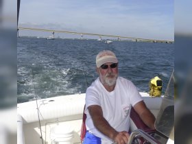 A man enjoys a day of fishing while steering a boat, with a bridge in the background — perfect for water enthusiasts and fishing adventures.