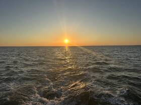 A stunning sunset over the open water, capturing the serene beauty of a boat's journey at dusk.