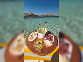 A beautifully arranged platter featuring cheese, cured meats, and cocktails, perfect for enjoying on a boat in crystal-clear waters.
