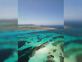 A stunning aerial view of a vibrant turquoise coastline, showcasing the natural beauty of the island and its surrounding waters — perfect for eco tours and scenic boat trips.