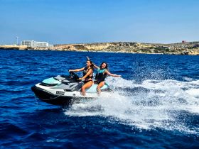 Two friends enjoy an exhilarating ride on a jet ski, creating splashes in the vibrant blue waters — a perfect snapshot of summer fun and adventure.