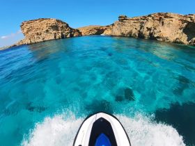 A thrilling view from a jet ski navigating through crystal-clear turquoise waters, showcasing stunning coastal rock formations — perfect for adventure seekers exploring the beauty of the sea.