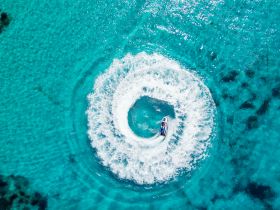 An exhilarating aerial view of a jet ski creating a circular wake in the stunning turquoise waters, showcasing the thrill of on-water activities.