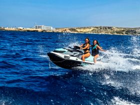 Two friends enjoy an exhilarating ride on a jet ski, splashing through the vibrant blue waters — a perfect snapshot of summer fun and adventure on the sea.