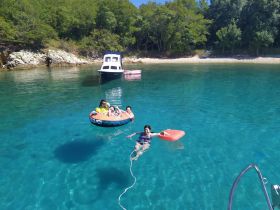 A joyful group enjoys a day of swimming and tubing in crystal-clear waters, with a picturesque beach backdrop — perfect for family adventures.