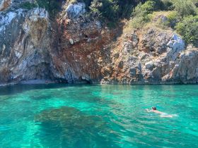 A swimmer enjoys the crystal-clear waters near a rocky coastline, showcasing the stunning natural beauty of the area — perfect for adventurous outings and beach exploration.