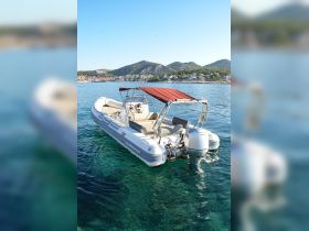 A sleek Clubman 24 speedboat anchored in crystal-clear waters, showcasing its elegant design against a picturesque coastal backdrop.