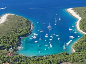 A stunning aerial view of a picturesque harbor filled with sailboats, surrounded by lush greenery and crystal-clear waters — a perfect destination for sailing enthusiasts.