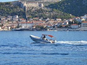 A small boat navigates through clear waters, showcasing a picturesque coastal town in the background — perfect for exploring the stunning scenery of the region.