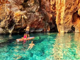 A family enjoys paddleboarding in crystal-clear waters near a stunning rocky cave, creating unforgettable memories in a picturesque setting.