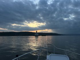 A serene sunset view featuring a lighthouse on the horizon, captured from a boat — perfect for showcasing tranquil moments on the water.