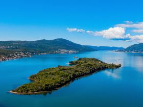 A stunning aerial view of a lush island surrounded by crystal-clear waters, showcasing the beautiful coastline and serene landscape, perfect for nature lovers and boating enthusiasts.