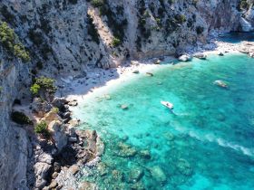 A stunning aerial view of a beach with sunbathers enjoying the turquoise waters, complemented by a boat cruising along the coastline — a perfect representation of a summer getaway.
