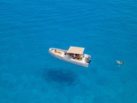 A lively group enjoys a day on the water aboard a boat, with one person snorkeling nearby in the vibrant blue sea — a perfect scene for aquatic adventures.
