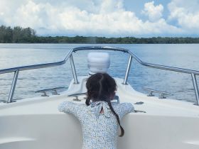 A young girl enjoys the serene view from the bow of a boat, surrounded by calm waters and lush greenery — a perfect moment for family adventures on the water.