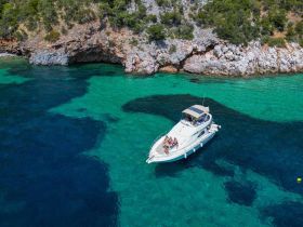 A lively group enjoys a day on the water aboard a boat, surrounded by stunning turquoise waters and rocky cliffs — perfect for summer adventures and beach outings.