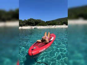 A young girl relaxes on a paddleboard in crystal-clear waters, enjoying a sunny day at the beach — a perfect scene for summer fun and water activities.