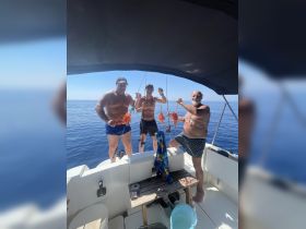 A group of three men proudly display their catch while fishing on a boat in the open ocean, showcasing a fun and successful day on the water.