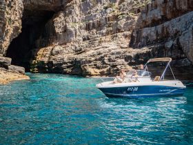 A group enjoys a scenic boat ride near a stunning cave, showcasing the beauty of the coastline and crystal-clear waters.