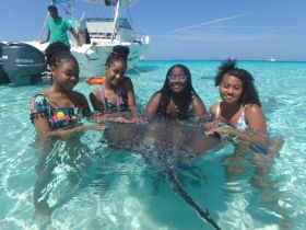 A group of girls interacts with a stingray in shallow turquoise waters, creating a memorable wildlife experience in the Bahamas.
