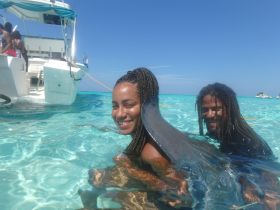A couple enjoys a refreshing swim in crystal-clear waters, with a boat anchored nearby — a perfect moment for adventure and relaxation on the water.