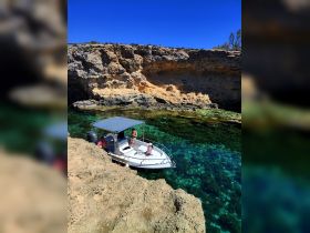 A group enjoys a sunny day on a boat near a rocky coastline, showcasing the beauty of clear waters and outdoor adventure.