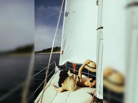A couple enjoys a relaxing moment on the deck of a sailboat, basking in the sun and surrounded by serene waters — perfect for a romantic getaway.