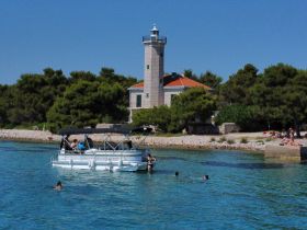 A lively scene featuring a group enjoying a pontoon boat while swimming near a picturesque lighthouse — a perfect summer getaway.
