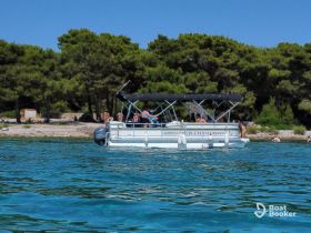 A lively group enjoys a sunny day on a pontoon boat, with beachgoers in the background, perfect for summer excursions and water activities.