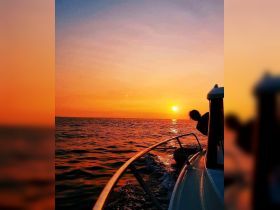 A stunning sunset view from a boat, with a silhouette of a person enjoying the serene waters — perfect for romantic evenings or peaceful escapes.