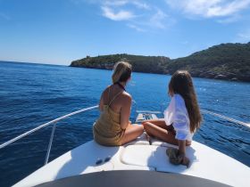 Two friends enjoy a serene moment on the bow of a boat, gazing at the stunning coastal scenery — a perfect escape for relaxation and adventure on the water.