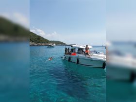 A lively scene of guests enjoying a swim in crystal-clear turquoise waters, with a boat anchored nearby, perfect for summer adventures and group outings.