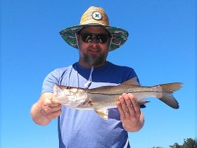 A proud angler displays his catch of the day, showcasing a beautiful fish against a clear blue sky — perfect for fishing enthusiasts and outdoor adventures.