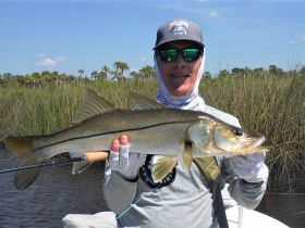 An angler proudly displays a freshly caught snook, showcasing the thrill of fishing in a scenic waterway surrounded by lush vegetation.