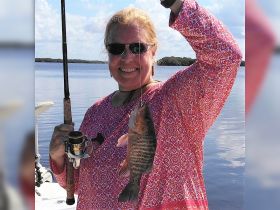 A joyful angler proudly displays her catch while fishing on calm waters, capturing the thrill of outdoor adventures.