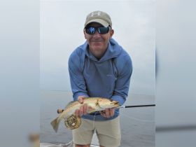 A man proudly displays his catch while fishing on a boat, showcasing the thrill of outdoor fishing adventures.