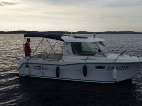 A well-maintained Ocqueteau 7.15 boat is docked on calm waters, with a person standing on deck, showcasing the vessel's design and features.