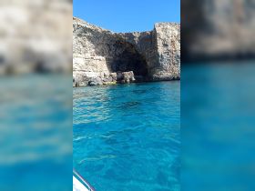 A stunning view of a natural cave along a rocky coastline, surrounded by crystal-clear turquoise waters — perfect for exploring scenic destinations by boat.