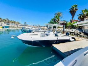 A sleek center console boat docked in a serene marina, surrounded by palm trees and clear blue waters, perfect for a day of fishing or leisure on the water.