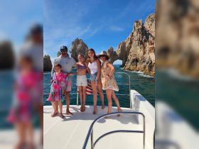 A joyful family poses on the deck of a boat in Cabo San Lucas, with stunning rock formations in the background — a perfect moment capturing their adventure on the water.