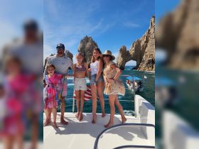 A joyful family poses on the deck of a boat in Cabo San Lucas, with stunning rock formations in the background — perfect for memorable family outings and sightseeing adventures.